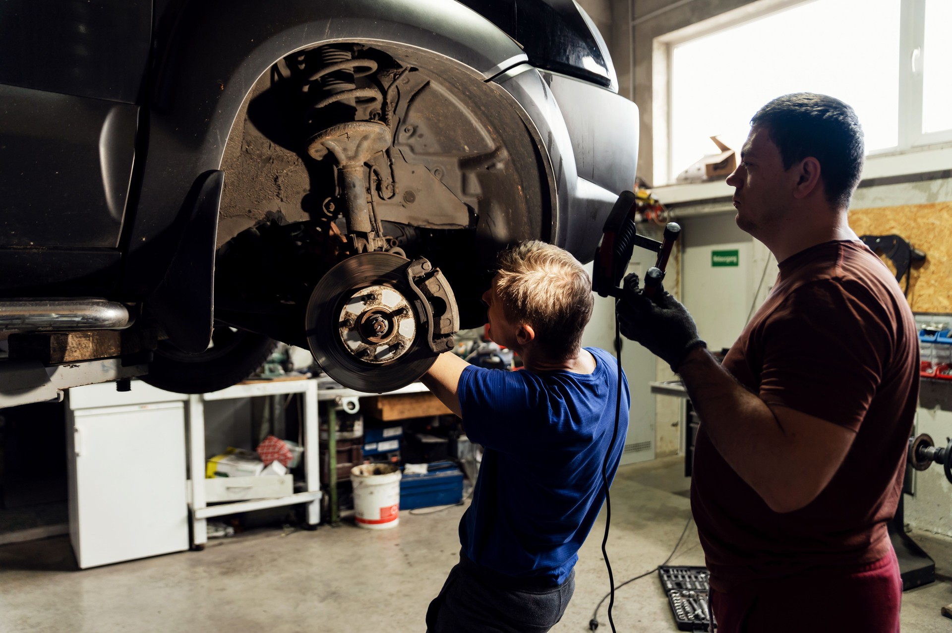 Professional mechanic inspects the brake system. assistant master illuminates the place of failure. repair the breakdown in the car. car brake repair service. replacement of pads and brake disc