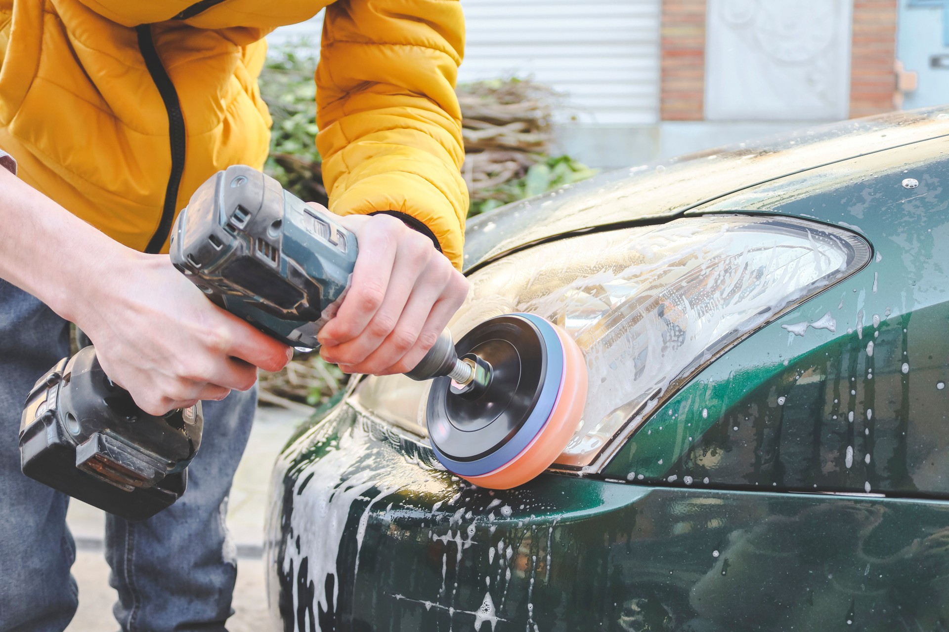 The hands of a young caucasian guy are drilling a drill with a disk with a sponge and polishing the headlight
